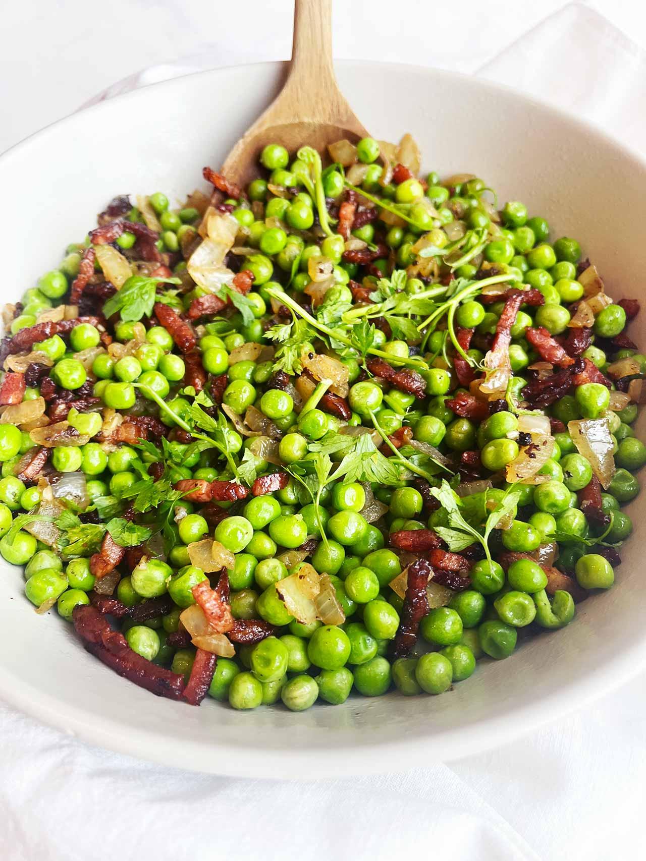 Font view. A white bowl with a wood spoon in it, filled with pea salad.