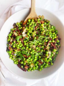 Overhead focus. A white bowl with a wood spoon, filled with pea salad.