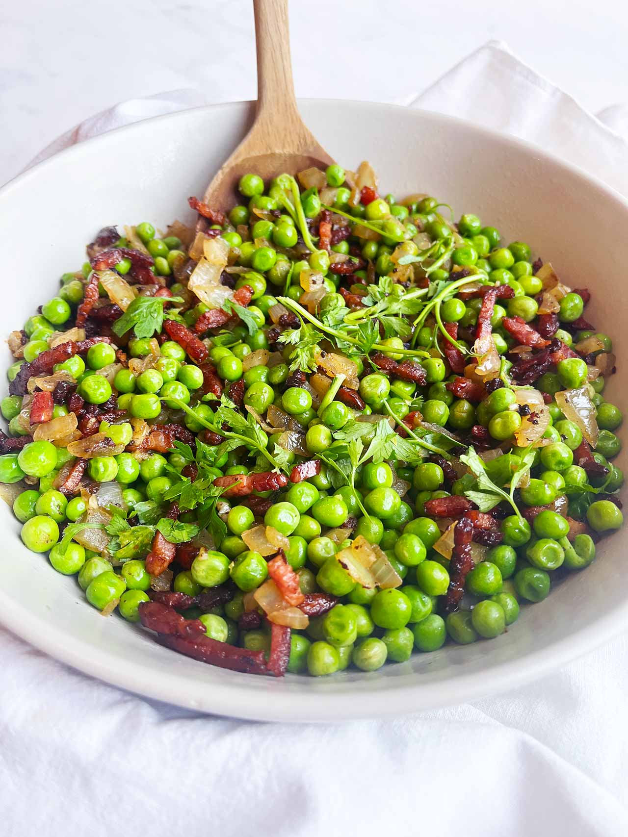 Front close up focus. A white bowl filled with pea salad.