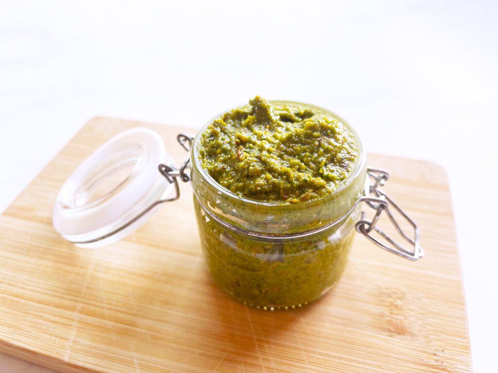 Pesto transferred from a food processor to a storage jar.