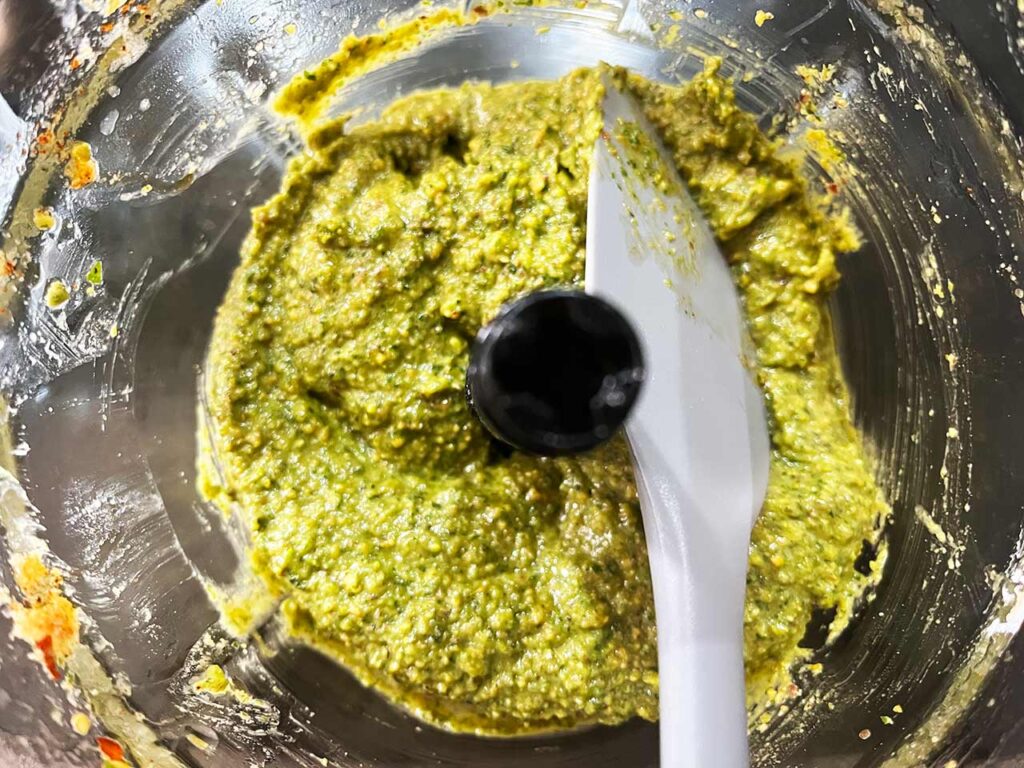 Blending pistachio pesto until smooth and adjusting with water to get the proper consistency.