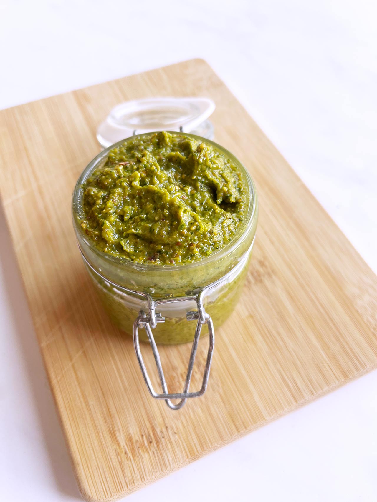 Slight overhead view of an open, glass jar filled with pistachio pesto.