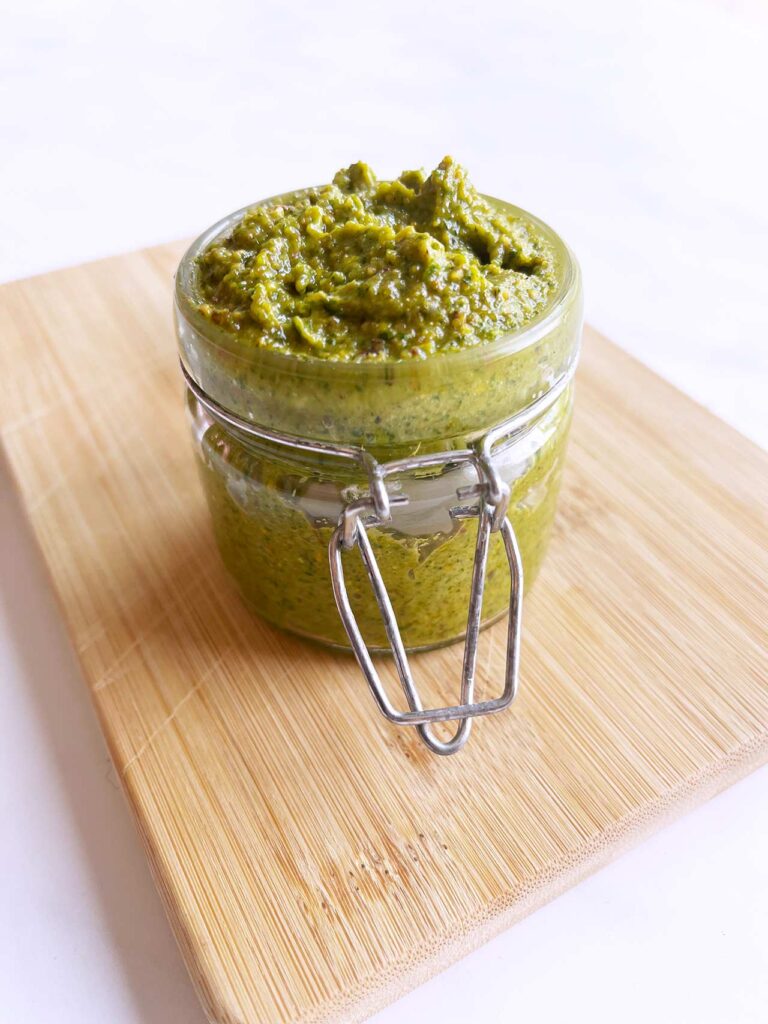 Front view of an open, glass jar filled with pistachio pesto.