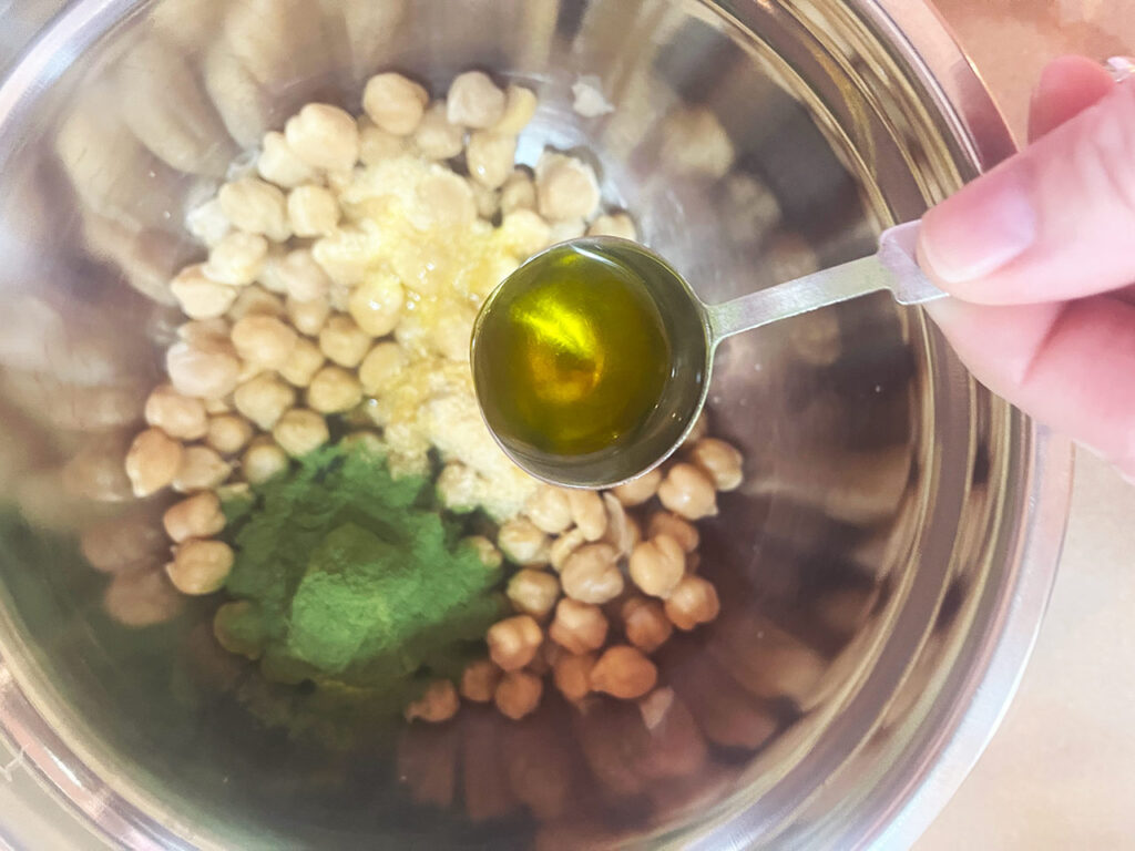 Adding oil to chickpeas and spices in a mixing bowl.
