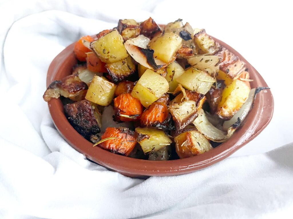 A brown dish on a white background, filled with sheet pan roasted vegetables.