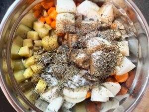 Spices added to potatoes, carrots, and onions in a mixing bowl.