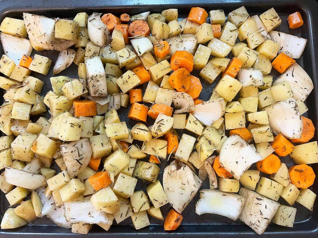 Potatoes, carrots, and onions spread out over a baking pan.