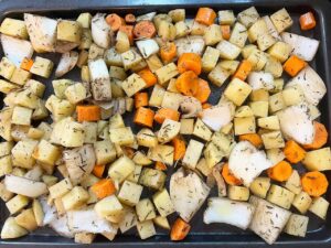 Potatoes, carrots, and onions spread out over a baking pan.