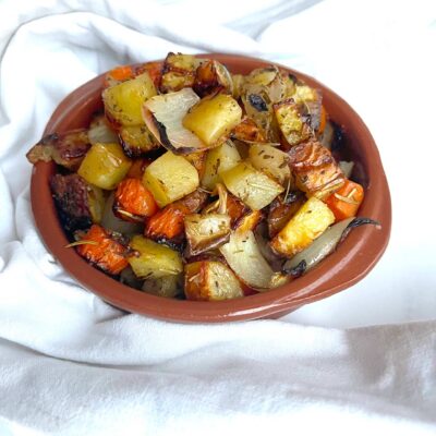 Front, angled view of a brown bowl filled with sheet pan roasted vegetables.