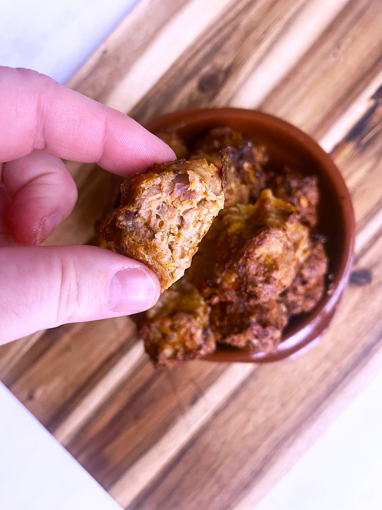 A hand lifts a single Smokey Pumpkin Turkey Meatball from the plate and shows it broken open.