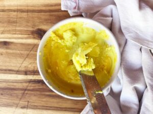 Overhead focus. A knife scoops out some vegan butter from a white ramekin.