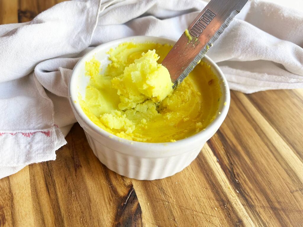 Front view. A knife scoops out some vegan butter from a white ramekin.