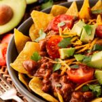 Closeup and partial view of a bowl of chili nachos.