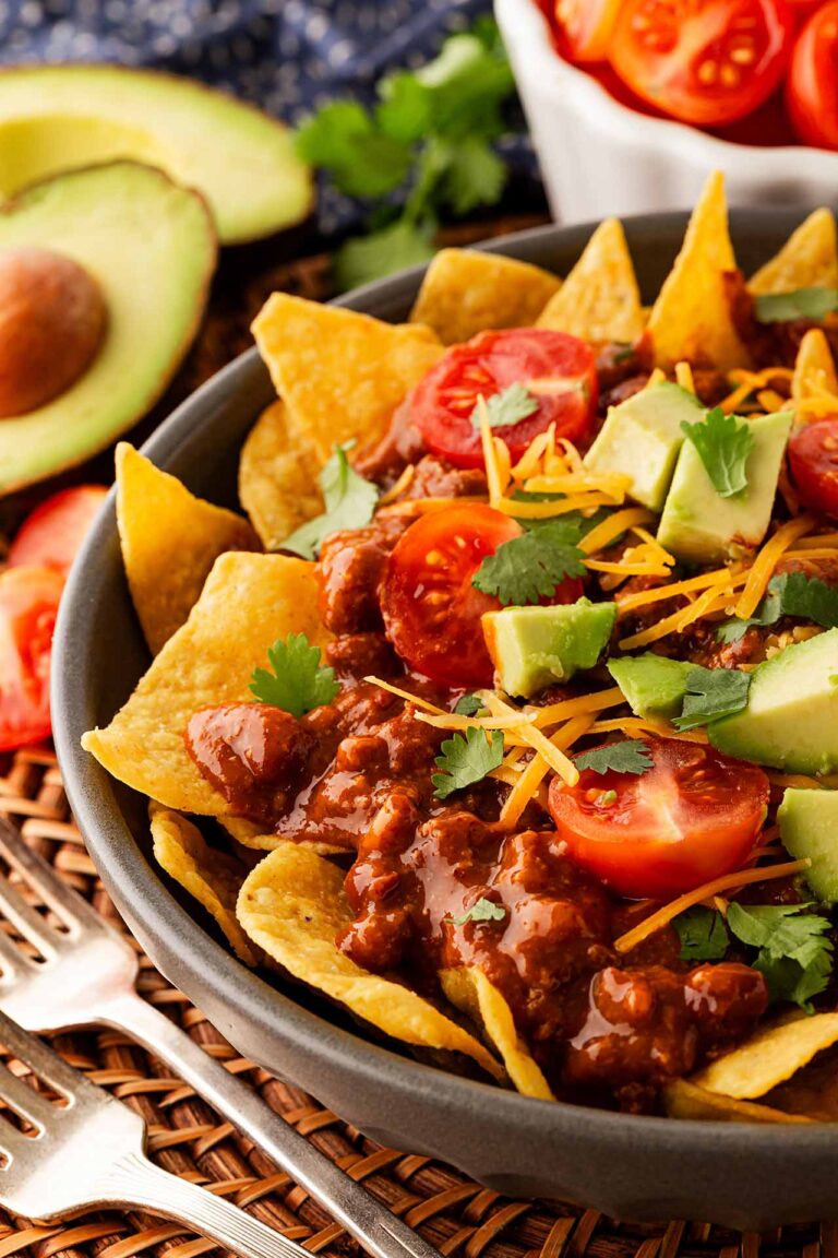 Closeup and partial view of a bowl of chili nachos.