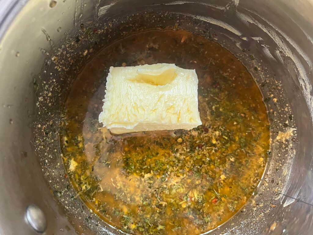 Half a stick of butter added to cooling melted butter and spices in a pot.