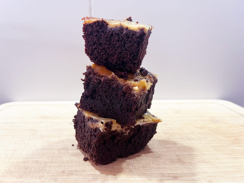 Three Cream Cheese Brownies stacked up on a wood cutting board.