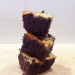 Front view of three Cream Cheese Brownies stacked up on a wood surface.