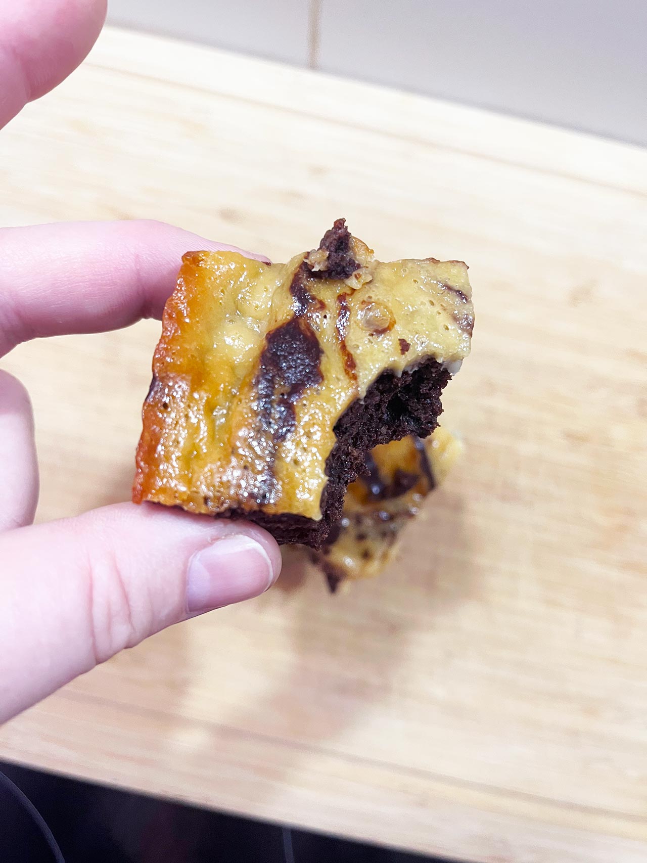 A hand holds a Cream Cheese Brownie with a bit taken from it.