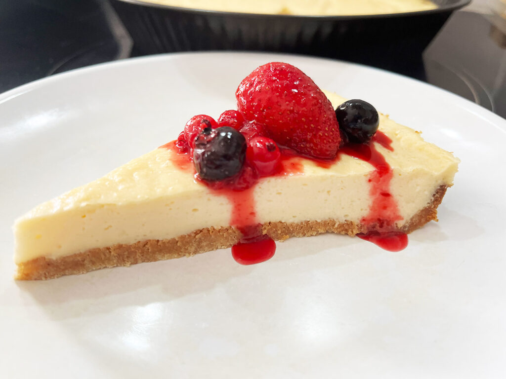 A slice of Custard Pie on a white plate, topped with berries and sauce.