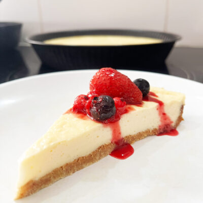 Eye level focus. A slice of Custard Pie on a white plate with berries and sauce on it.