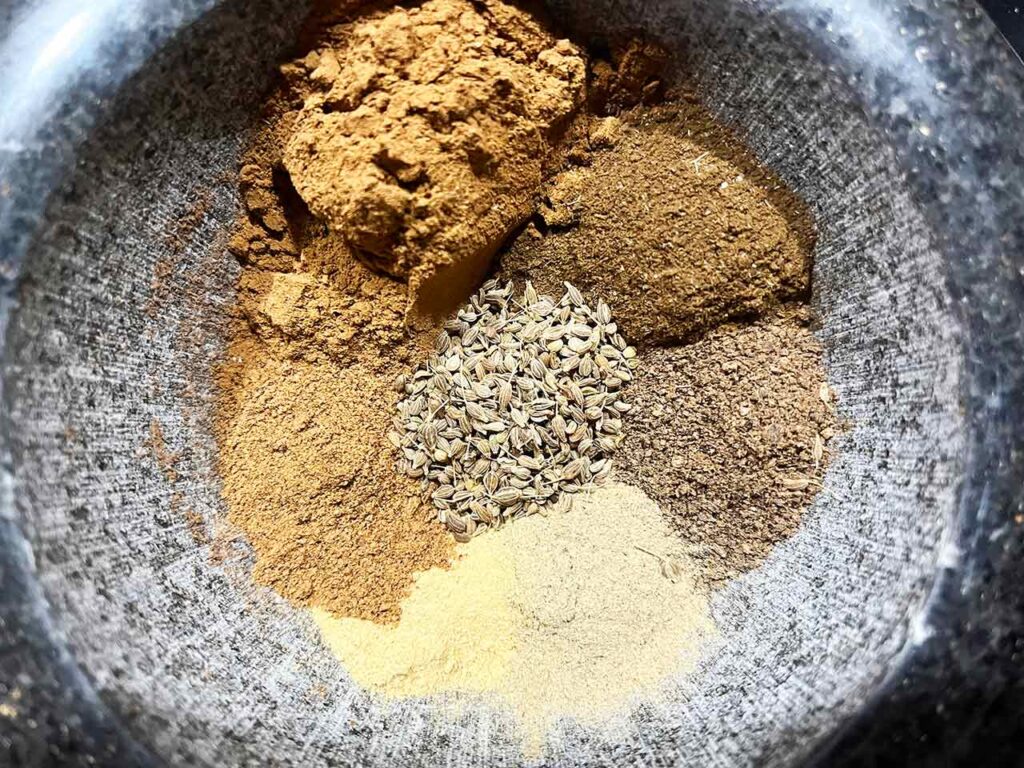 Individual ingredients for gingerbread spice placed in a mortar for mixing.