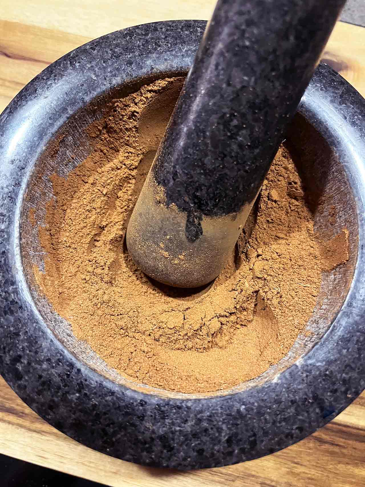 Overhead focus. A mortar filled with gingerbread spices. A pestle rests in the spices.