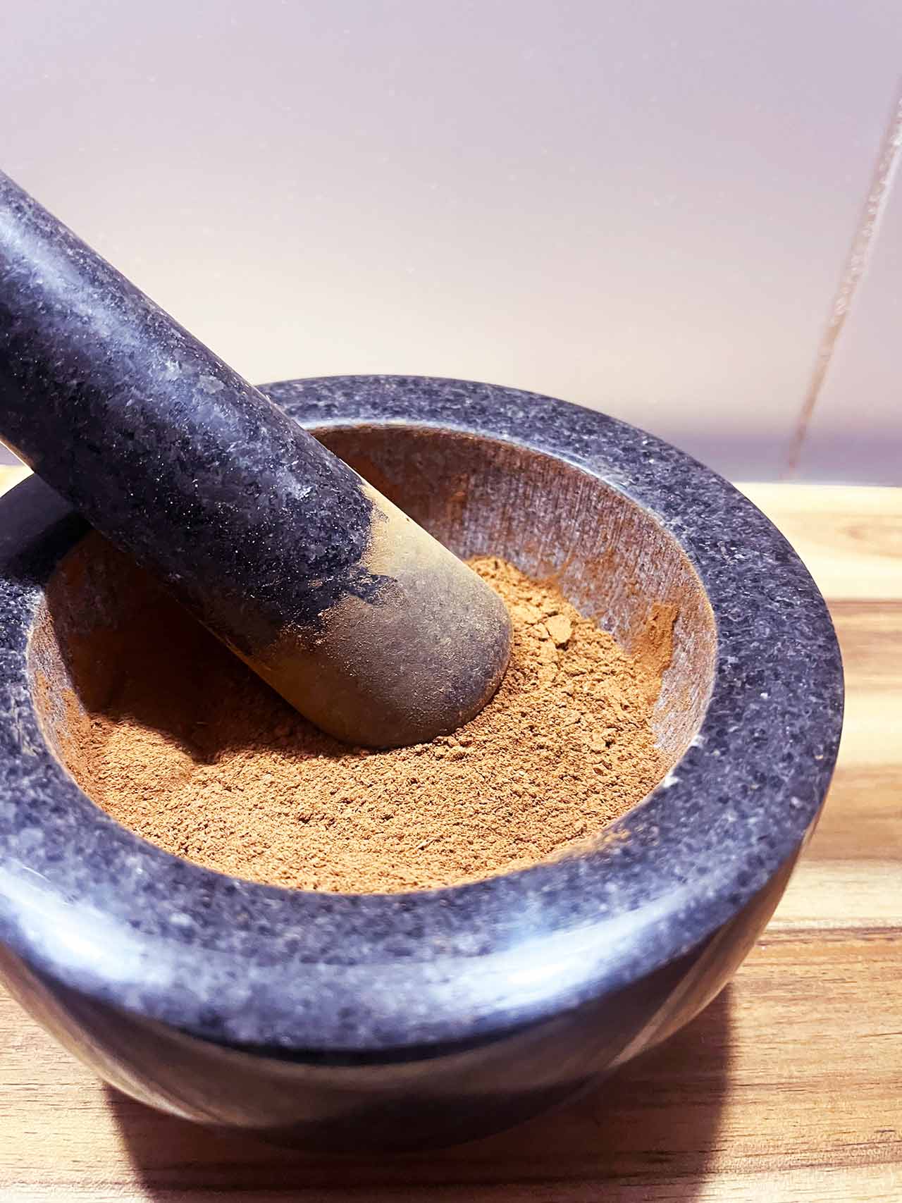 A mortar and pestle with gingerbread spice on a wood surface.