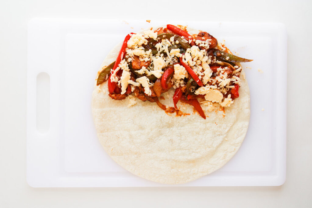 Cheese added to fajita mix on a tortilla.