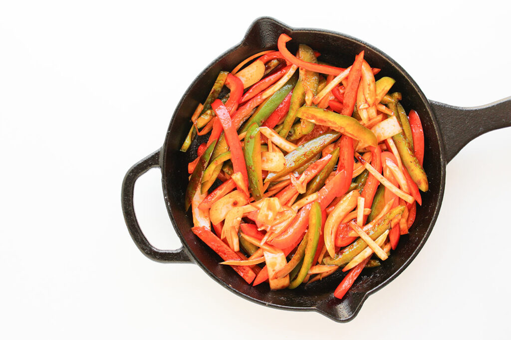 Raw peppers and onions in a skillet.