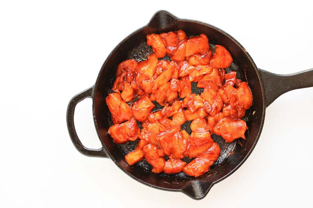Raw chicken chunks in a skillet.