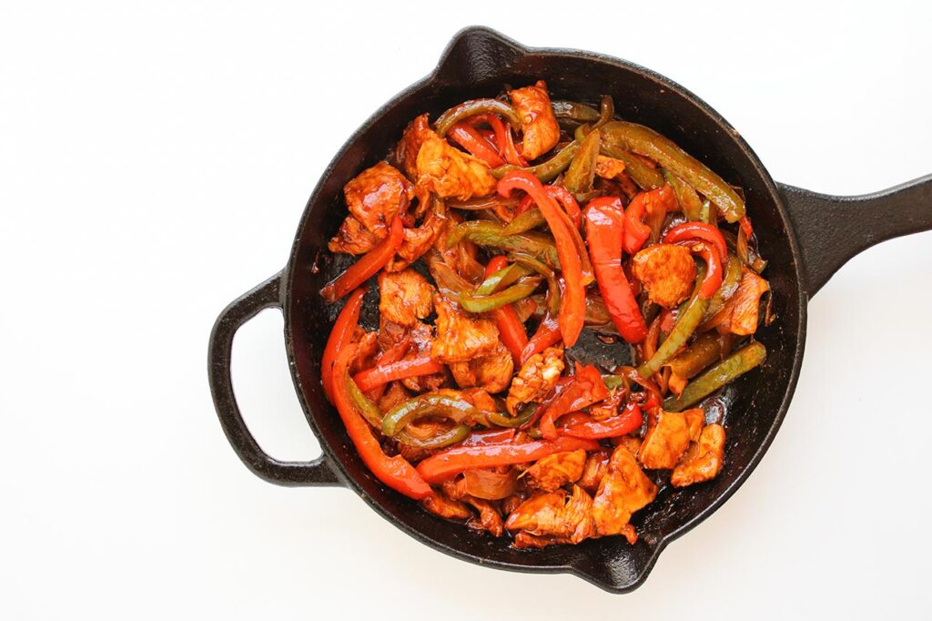 Cooked chicken, peppers and onions mixed together in a skillet.