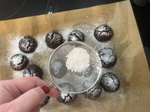 Sprinkling extra powdered sweetener over Oat Flour Chocolate Crinkle Cookies.