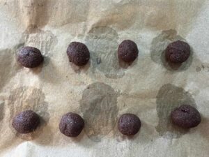 Balls of Oat Flour Chocolate Crinkle Cookie dough on a parchment-lined cookie sheet.
