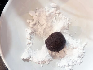 Rolling a Oat Flour Chocolate Crinkle Cookie dough ball in powdered sweetener.