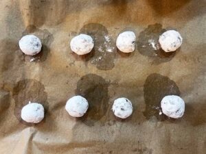 Oat Flour Chocolate Crinkle Cookie dough balls rolled in powdered sweetener sitting on a parchment-lined baking pan. Overhead focus.