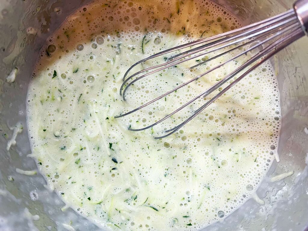 Wet ingredients for Chocolate Zucchini Bread whisked together in a mixing bowl. A whisk rests in the bowl.