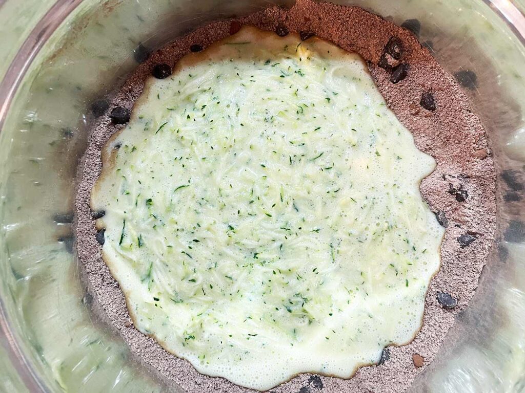 Wet and dry ingredients for Chocolate Zucchini Bread in a mixing bowl.