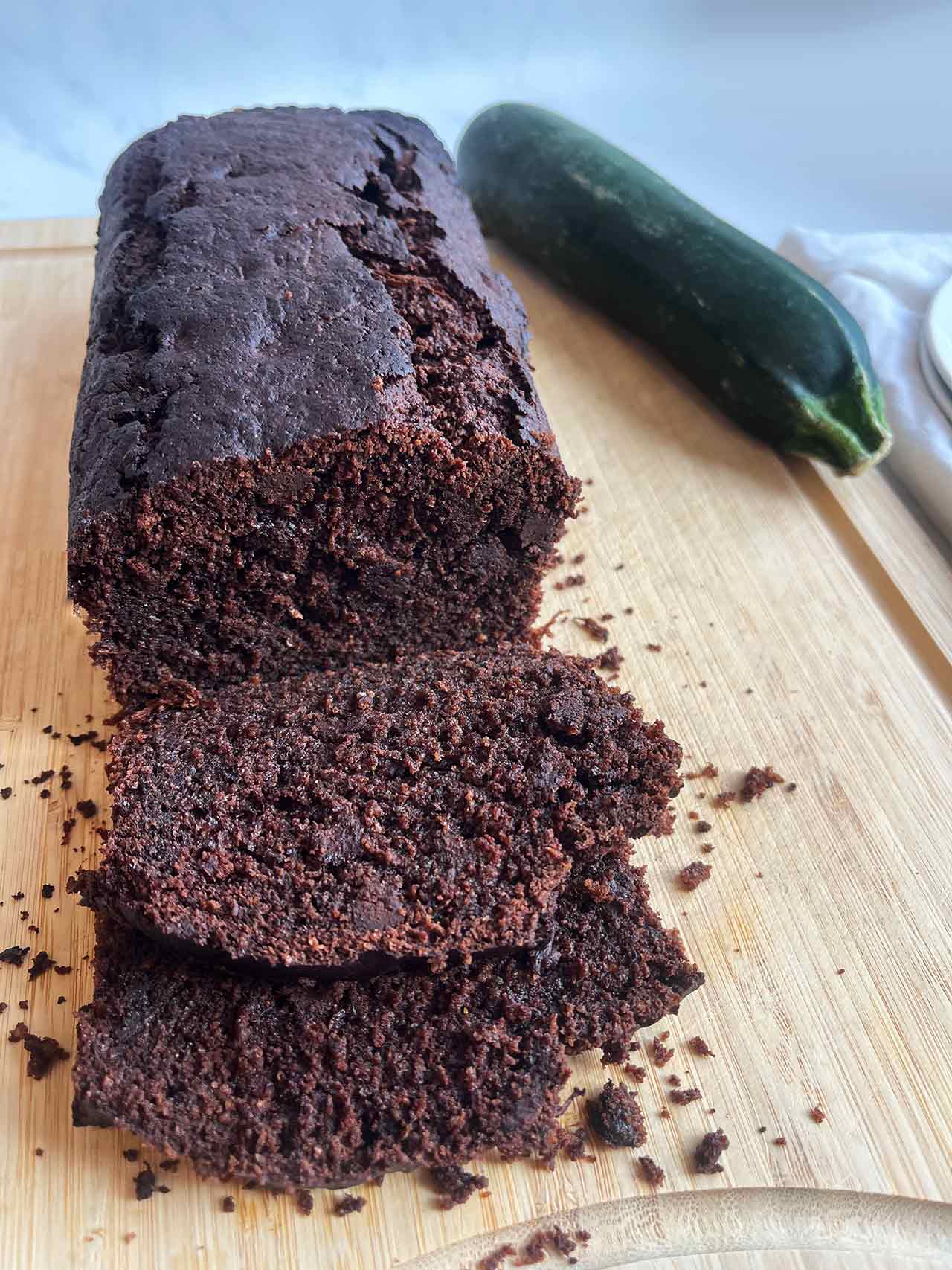 Front view of a chocolate zucchini bread loaf on a cutting board next to a raw zucchini.
