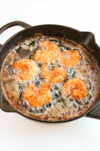 Crispy Coconut Shrimp frying in oil in a skillet.