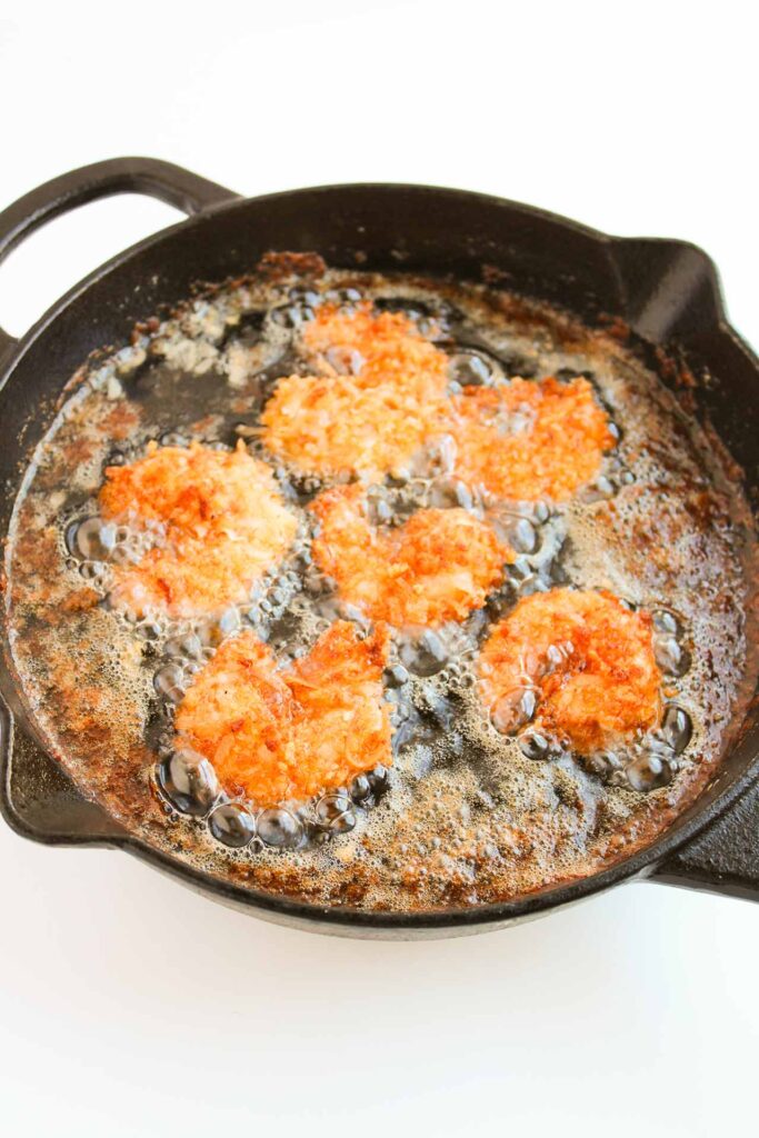 Crispy Coconut Shrimp frying in oil in a skillet.