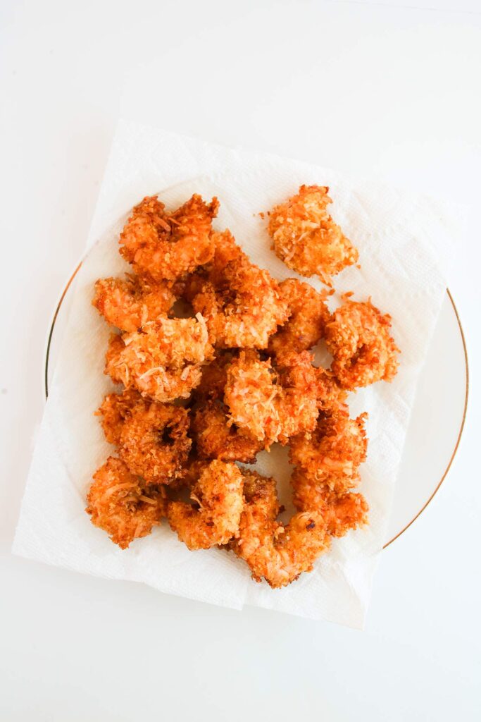 Overhead focus. Crispy Coconut Shrimp laying on a paper towel-lined plate.