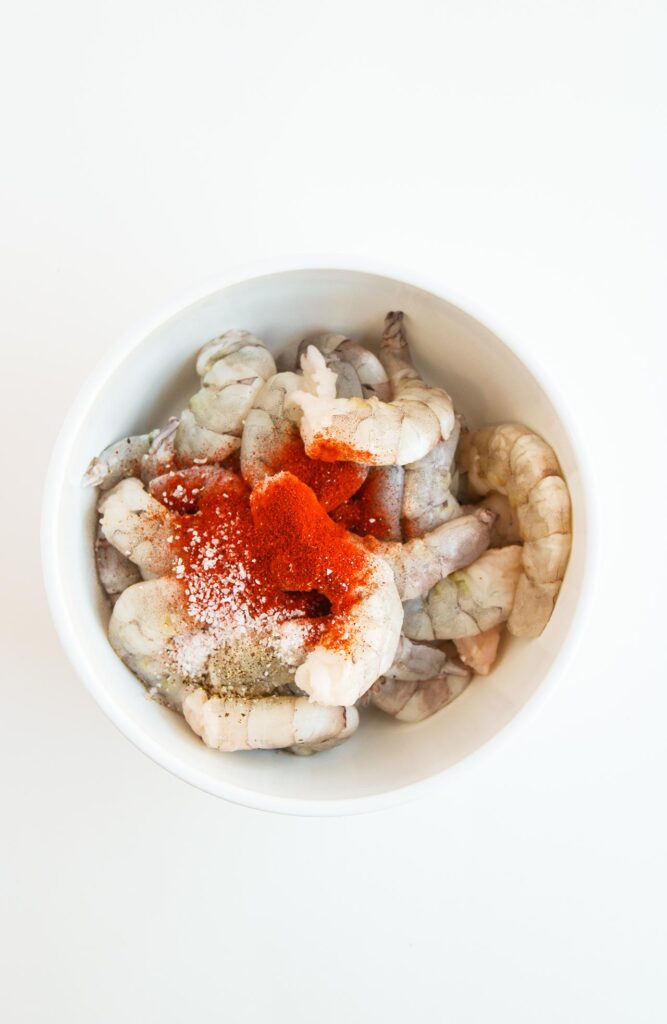Seasoning added to raw shrimp in a white bowl.