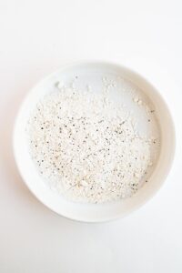 Flour with salt and pepper in a white bowl.