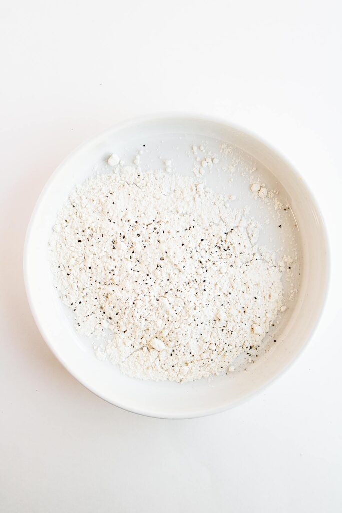 Flour with salt and pepper in a white bowl.