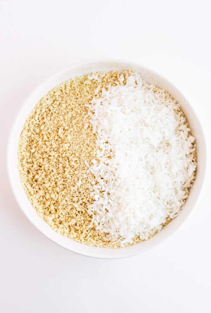 Coconut flakes added to bread crumbs in a white bowl.