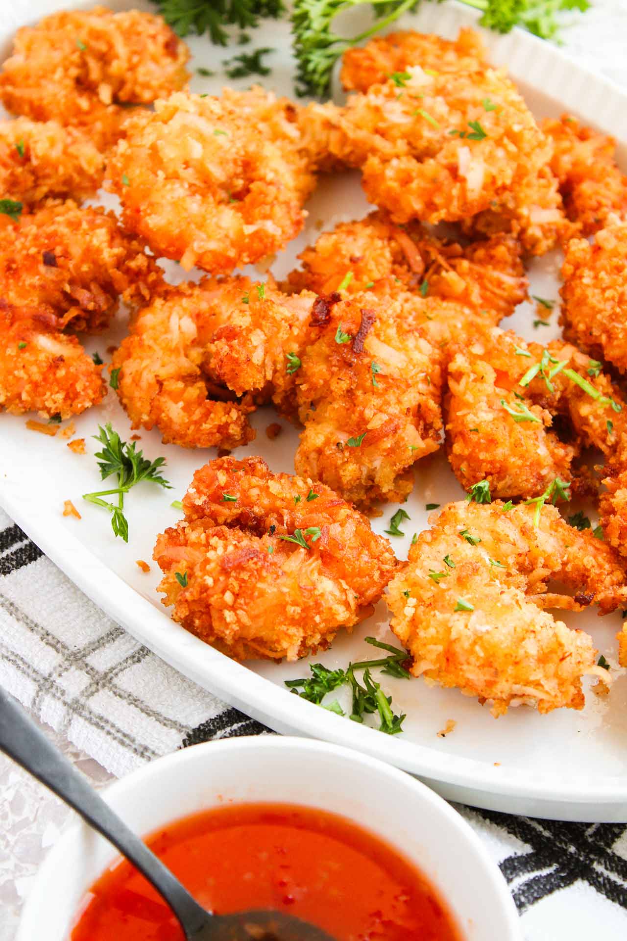 Crispy Coconut Shrimp on a white platter next to a bowl of chili sauce.