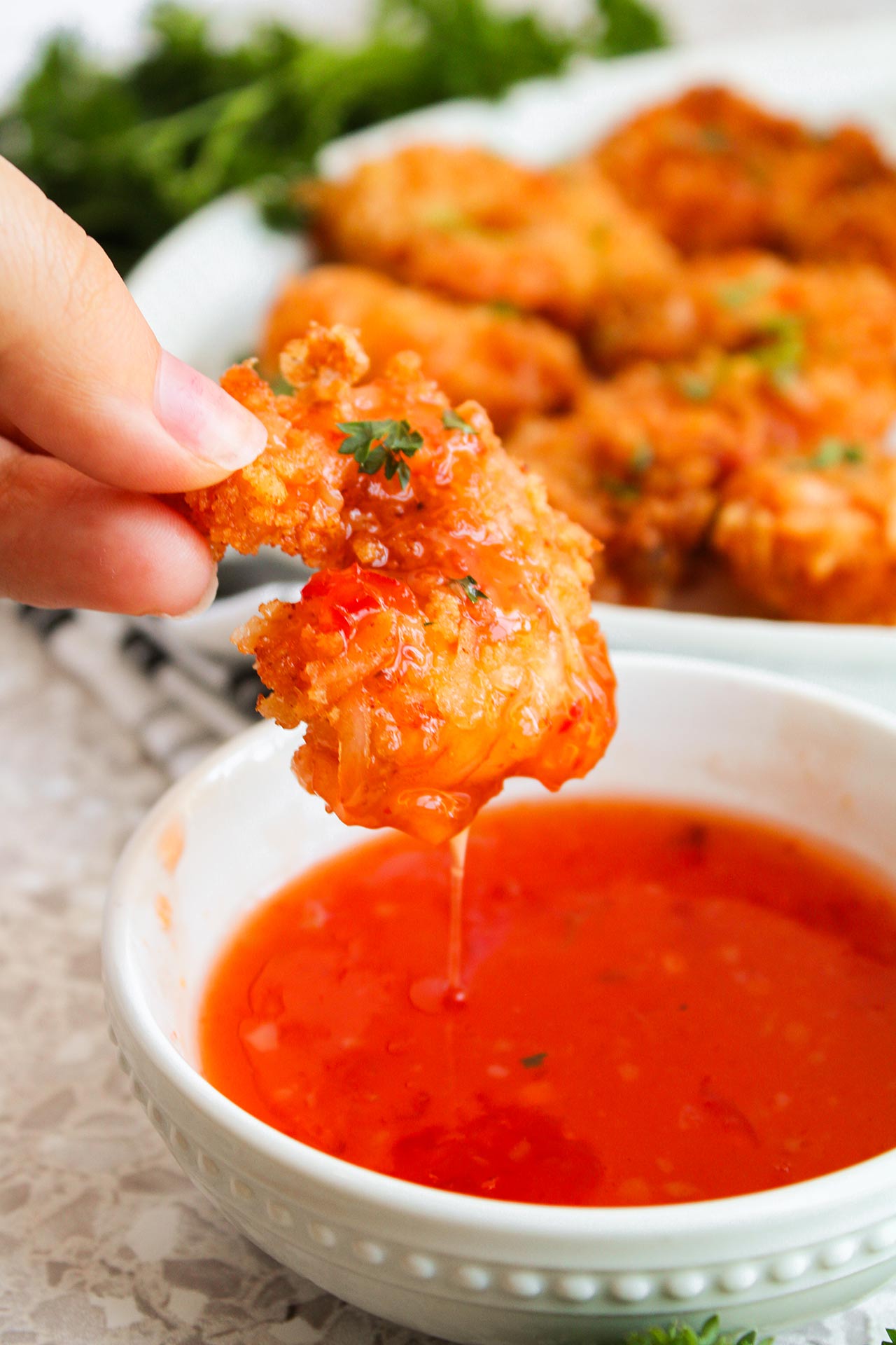 A hand holds a Crispy Coconut Shrimp just dipped in chili sauce