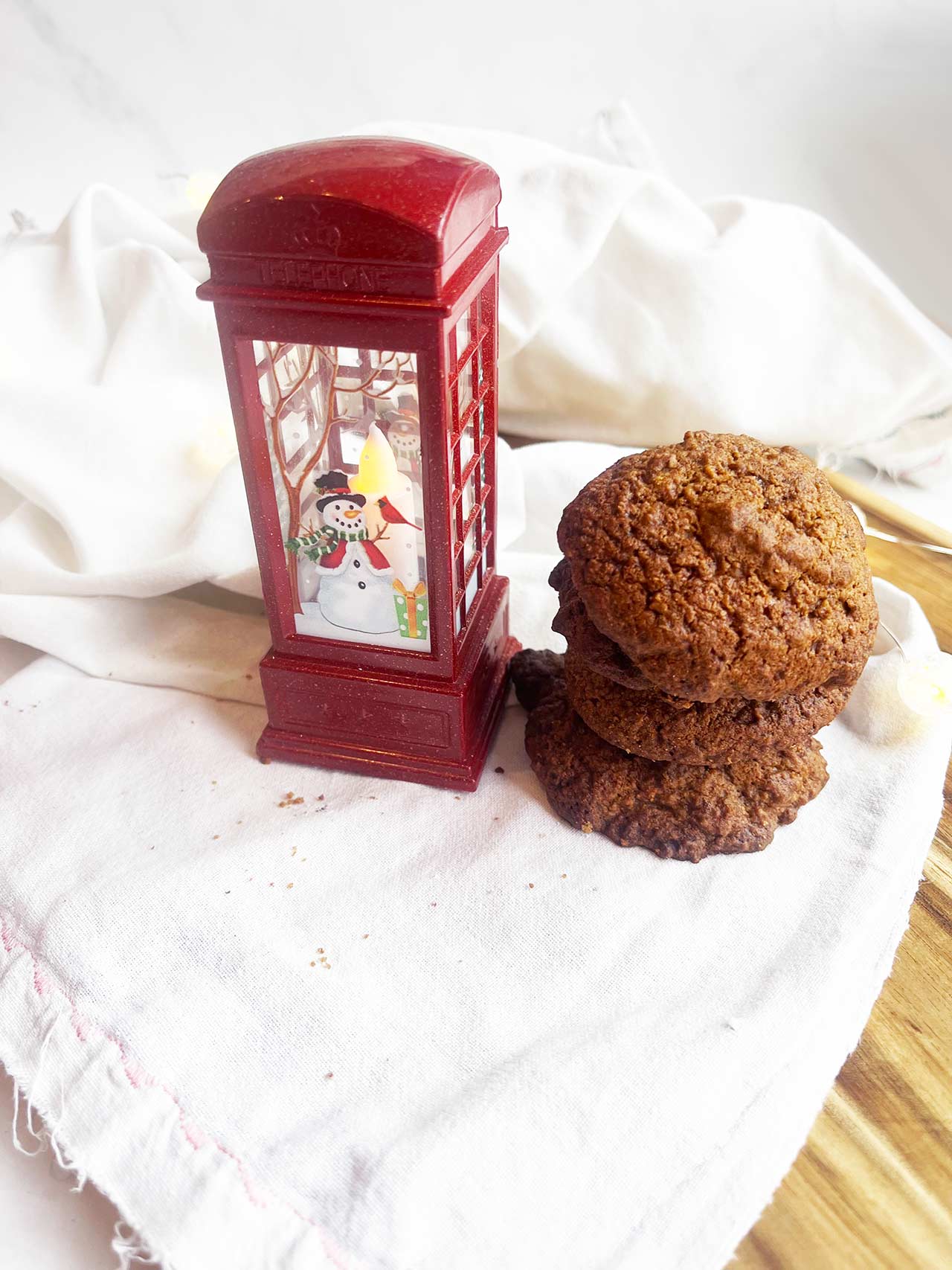 Front view of a stack of Oat Flour Ginger Molasses Cookies sitting next to a red phone booth ornament on a white towel.