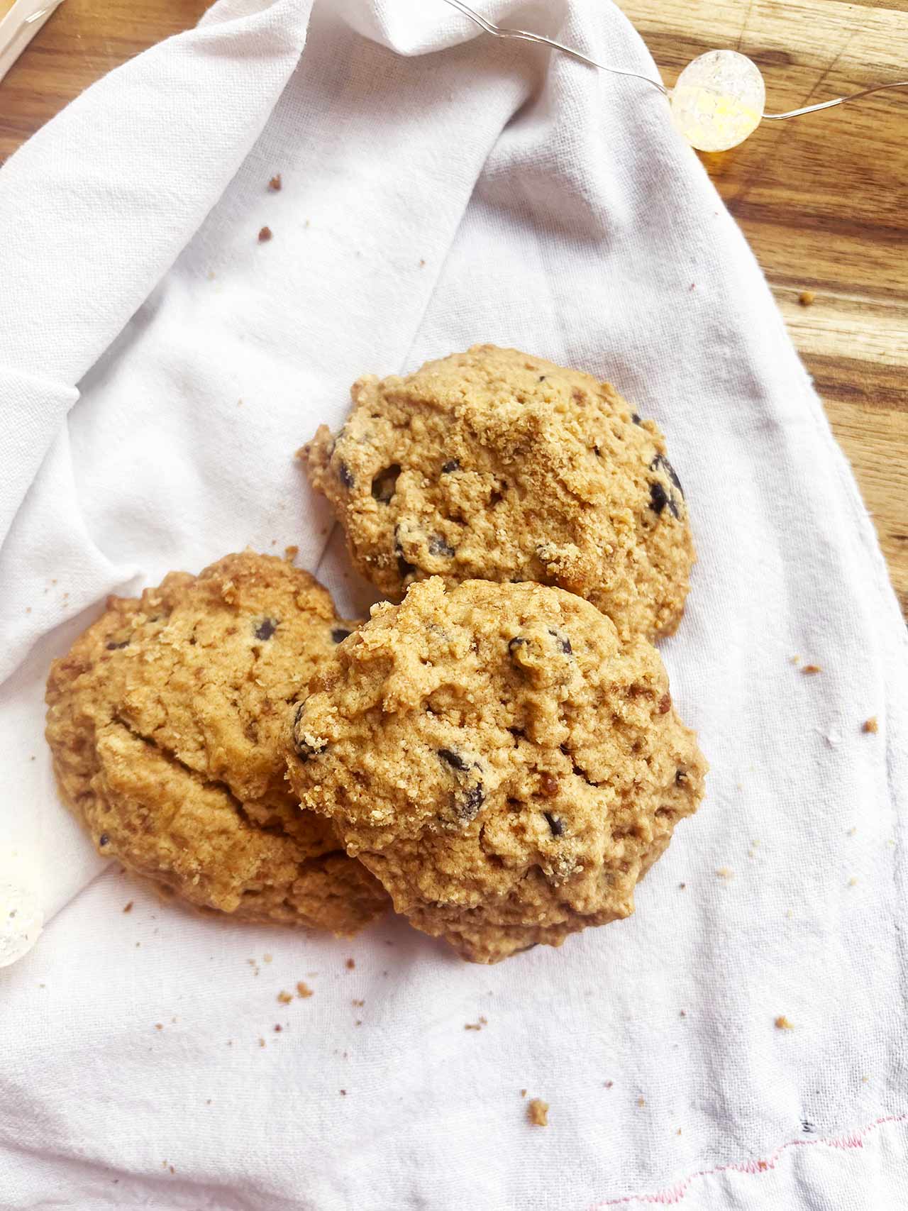 Overhead angled focus. Three Oat Flour Chocolate Chip Cookies on a white towel.