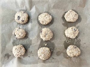 Oat Flour Oatmeal Raisin Cookies formed and laying on a parchment-lined baking pan.